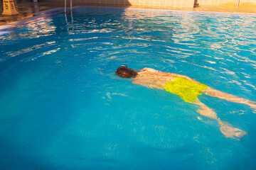 Close up view of boy swimming underwater in clear blue pool during sunny summer day. Spain.