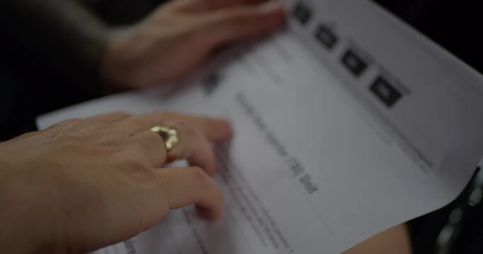 Close‑up of hands holding and flipping through blurred paperwork or contract, gold ring visible on finger, shallow depth of field emphasizing motion and document handling.