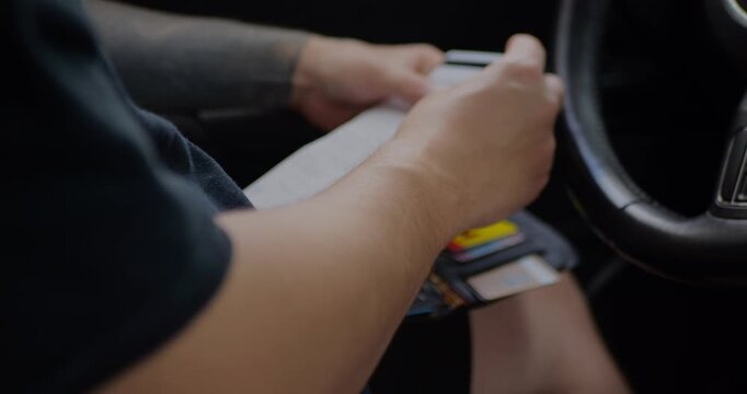Close-up of driver hands holding smartphone and stack of credit cards at steering wheel, preparing to pay or manage finances in car, mobile banking, online shopping and contactless payment concept.