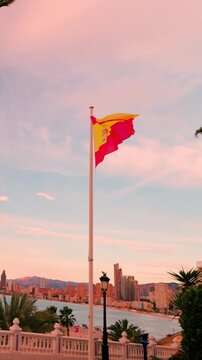 Spanish flag waving in the wind over benidorm cityscape at sunset