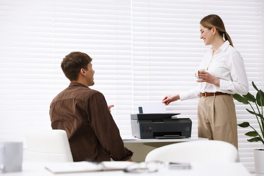 Smiling woman talking with her colleague at desk with printer in office