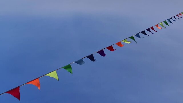 brightly colored pennant flags on string gently fluttering in wind against clear blue sky, symbolizing celebration, festivals, outdoor parties, and joyful summer events.