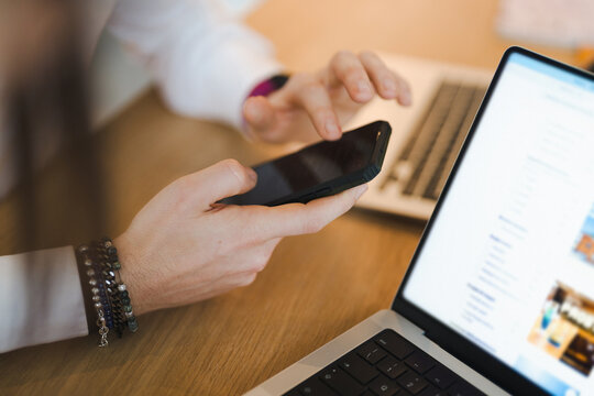 A person uses a smartphone and laptop to research travel options, browsing accommodation filters and booking details on a website.