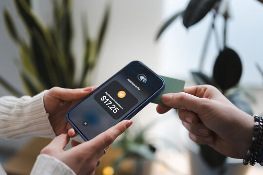 A person holds a smartphone displaying a payment screen, while another person uses a card to complete the transaction.