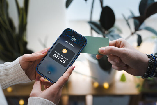A person holds a smartphone displaying a payment of $17.25 for a greenhouse purchase, while another person presents a card for contactless payment.