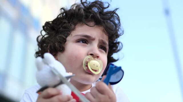 Armenian toddler wearing pacifier looking up with curly hair outdoors