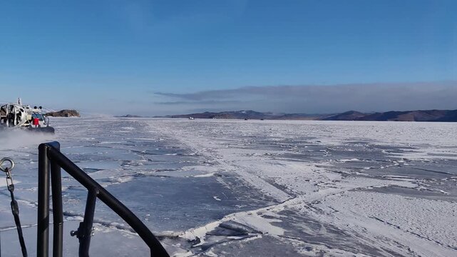 exciting journey aboard hovercraft traveling at high speed over cracked ice surface vast frozen lake baikal in siberia during sunny winter day with picturesque hills on horizon.