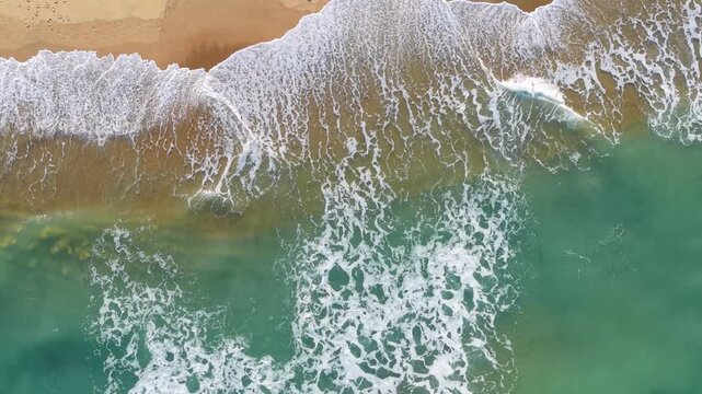 Kill Devil Hills, North Carolina, a top-down aerial view of turquoise Atlantic waters crashing against a sandy beach shoreline with tire tracks on the Outer Banks.