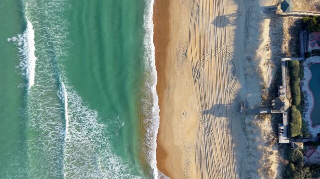 Kill Devil Hills, North Carolina, a top-down aerial view of turquoise Atlantic waters crashing against a sandy beach shoreline with tire tracks on the Outer Banks.