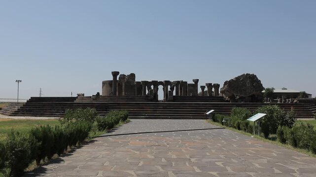 Explore the ancient ruins of Zvartnots Cathedral in Armenia. This beautiful historical site features stunning stone pillars and arches under a clear blue sky, showcasing remarkable medieval architectu
