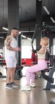 Senior woman exercising with chest press machine with professional trainer in gym