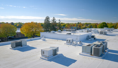 Obraz premium White flat roof with various air conditioning units and rooftop hvac systems in an urban setting