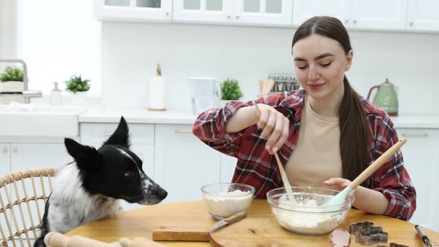 Woman making cookies near cute dog at wooden table in kitchen