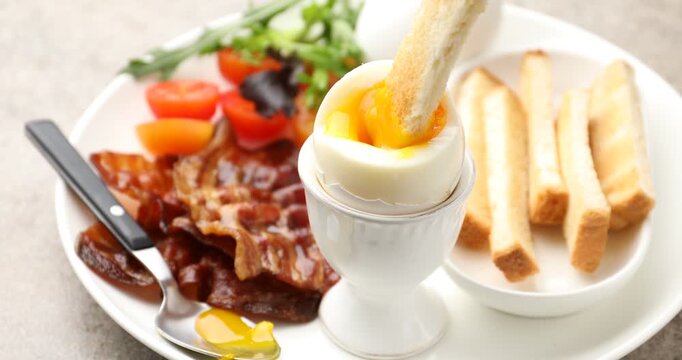 Tasty breakfast. Dipping toasted bread into soft boiled egg at grey table, closeup