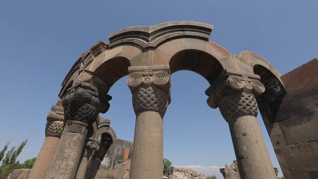 Explore the ancient ruins of Zvartnots Cathedral in Armenia. This beautiful historical site features stunning stone pillars and arches under a clear blue sky, showcasing remarkable medieval architectu
