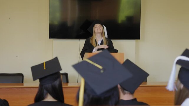 A young woman stands at the lectern and delivers a graduation speech to her classmates. 