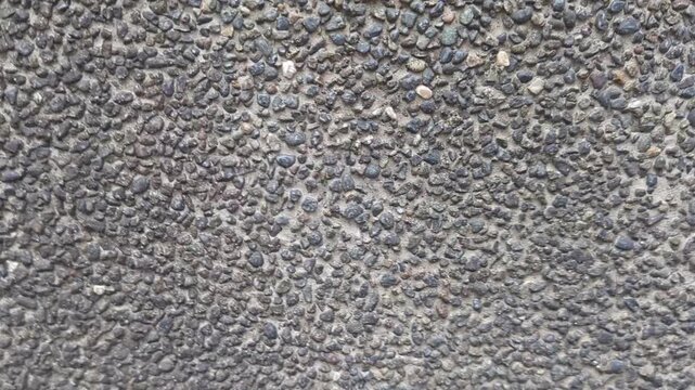 Slow motion close-up of grey washed pebble texture on a wall surface