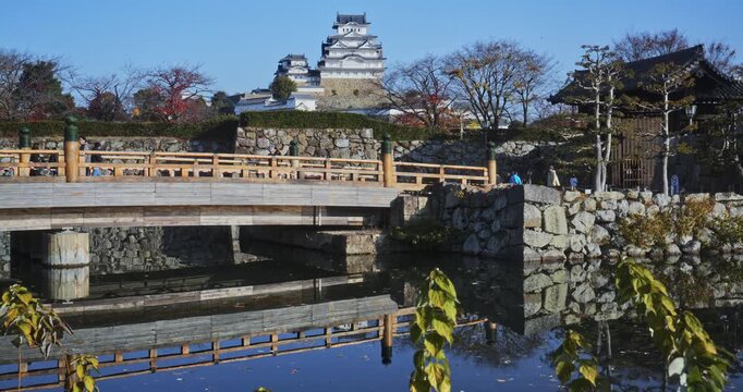 Beautiful, small bridge reflection in pond with ancient 16th century Japanese castle in distance - wide shot