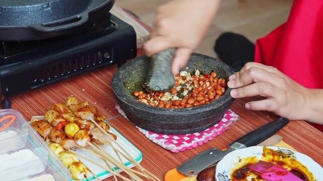 Hands grinding roasted peanuts in stone mortar (cobek) to make traditional Indonesian peanut sauce