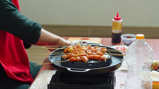 Close up hand Chef preparing traditional Indonesian chicken satay on portable indoor grill