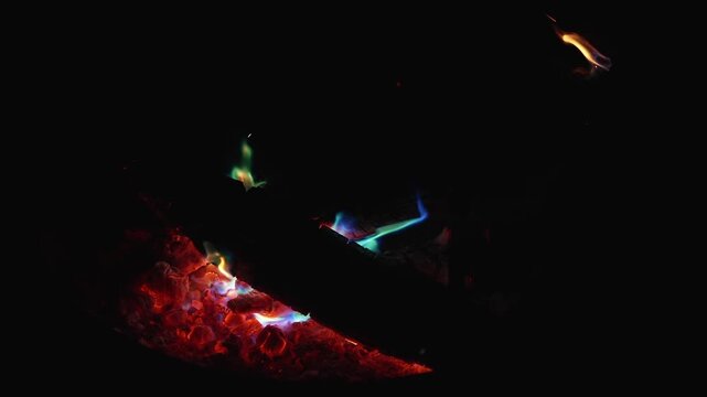 Slow flickering campfire with green flame tongues at night, recorded in slow motion at 120fps with vivid ember glow
