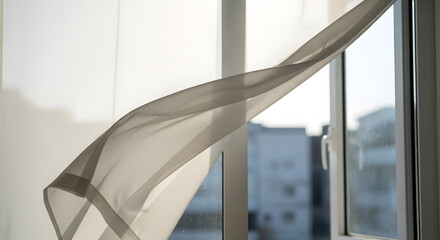 Fototapeta premium Soft fabric veil moving with the breeze against a blurred urban background in a bright airy room