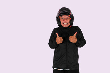 An expressive Indonesian man smiles on an isolated white background while giving a thumbs up (okay symbol) while wearing a helmet and jacket.