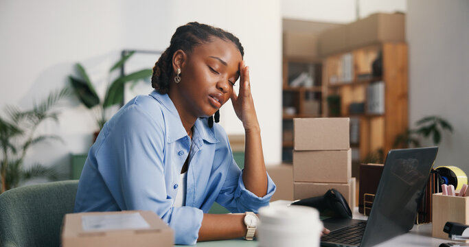 Ecommerce, woman and headache in office with laptop, logistics stress and bad review for distribution. Tired, black person and migraine in workplace with computer, courier delay and supplier backlog.