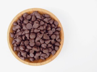 Fototapeta premium Chocolate chips are in a wooden cup placed on a white surface. It looks delicious and sweet.