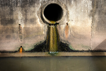 A concrete drainage pipe discharges polluted liquid and raw sewage into a river, staining the wall. A stark image of water contamination and environmental pollution in Brazil.