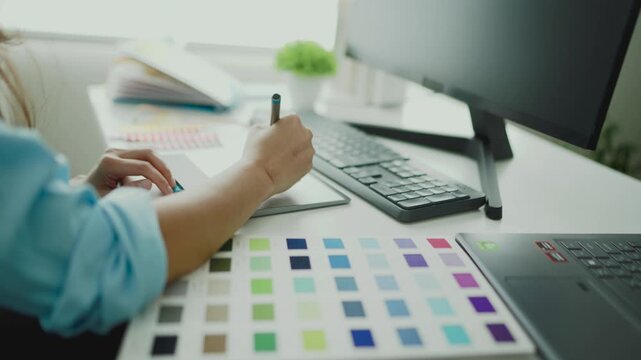 Female artist hands writing continuously on pad in digital art studio with multi monitor setup and black screens. Dynamic typing movement expressing creative process visual storytelling.
