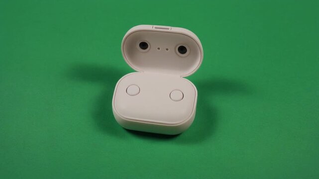 White wireless earbuds in an open charging case on a green background with shadows.