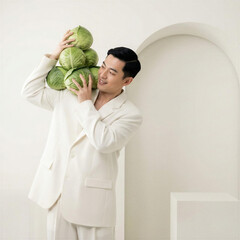 Asian male model posing while holding fresh green cabbages in white studio  