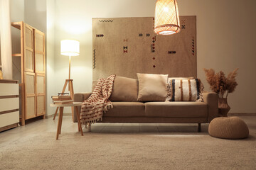 Interior of modern living room with grey sofa, glowing lamps and stylish carpet at evening