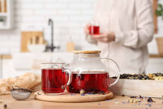 Teapot with healthy hibiscus tea and different herbs on table in kitchen