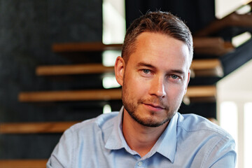 Obraz premium Man poses for a portrait indoors near wooden stair structure during a sunny day