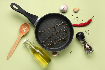Composition with frying pan, bottle of oil and spices on green background
