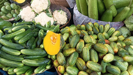 Fresh market display of various green vegetables and a sweet pumpkin