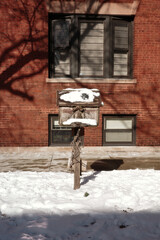 Weathered Birdhouse Covered in Snow in Front of Red Brick Building on a Winter Day