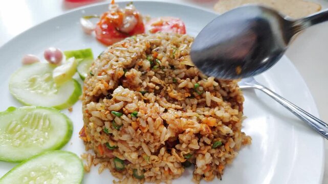 A plate of authentic indonesian fried rice served with freshly cut cucumber and tomato