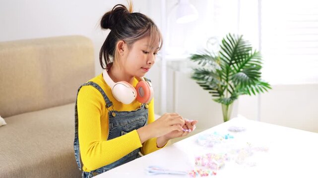Bead arts. Inspired tween girl enjoy hobby make handmade fashion jewelry from colorful plastic beads set stringing beads on strips in living room at home.