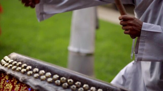 Person drumming on cultural instrument outdoors, energetic mood