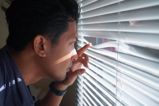 Curious man looking through venetian blind