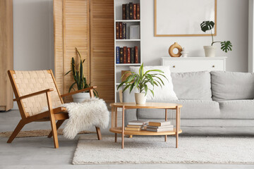 Bookcase, cozy sofa, coffee table and wicker armchair in interior of stylish living room. Blurred...