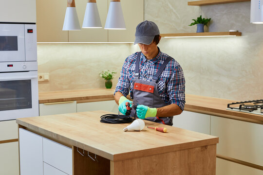Electrician wearing gloves using pliers, cutting wires for led lighting installation in modern kitchen