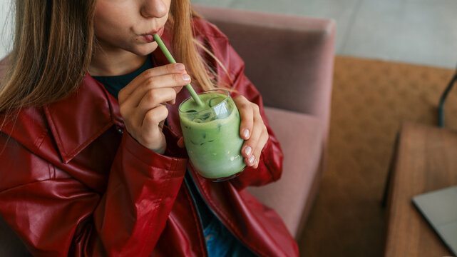 Young woman in a red leather jacket drinks a refreshing iced matcha latte with a reusable straw