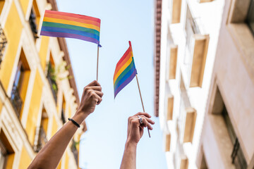 Hands holding rainbow flags high during a pride parade or celebration in a city street, advocating for lgbt rights and diversity