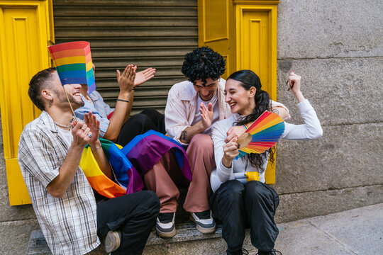 Diverse young people expressing joy and freedom at a pride festival, sitting outdoors with rainbow accessories