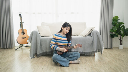 Fototapeta premium Young woman playing ukulele on living room floor, cozy atmosphere with plant and guitars, vibrant colors, relaxed setting, personal space, indoor lifestyle