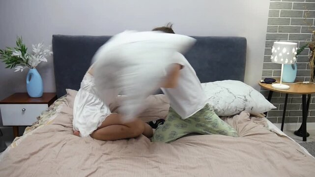 A young mother and her son are playing a pillow fight on the double bed